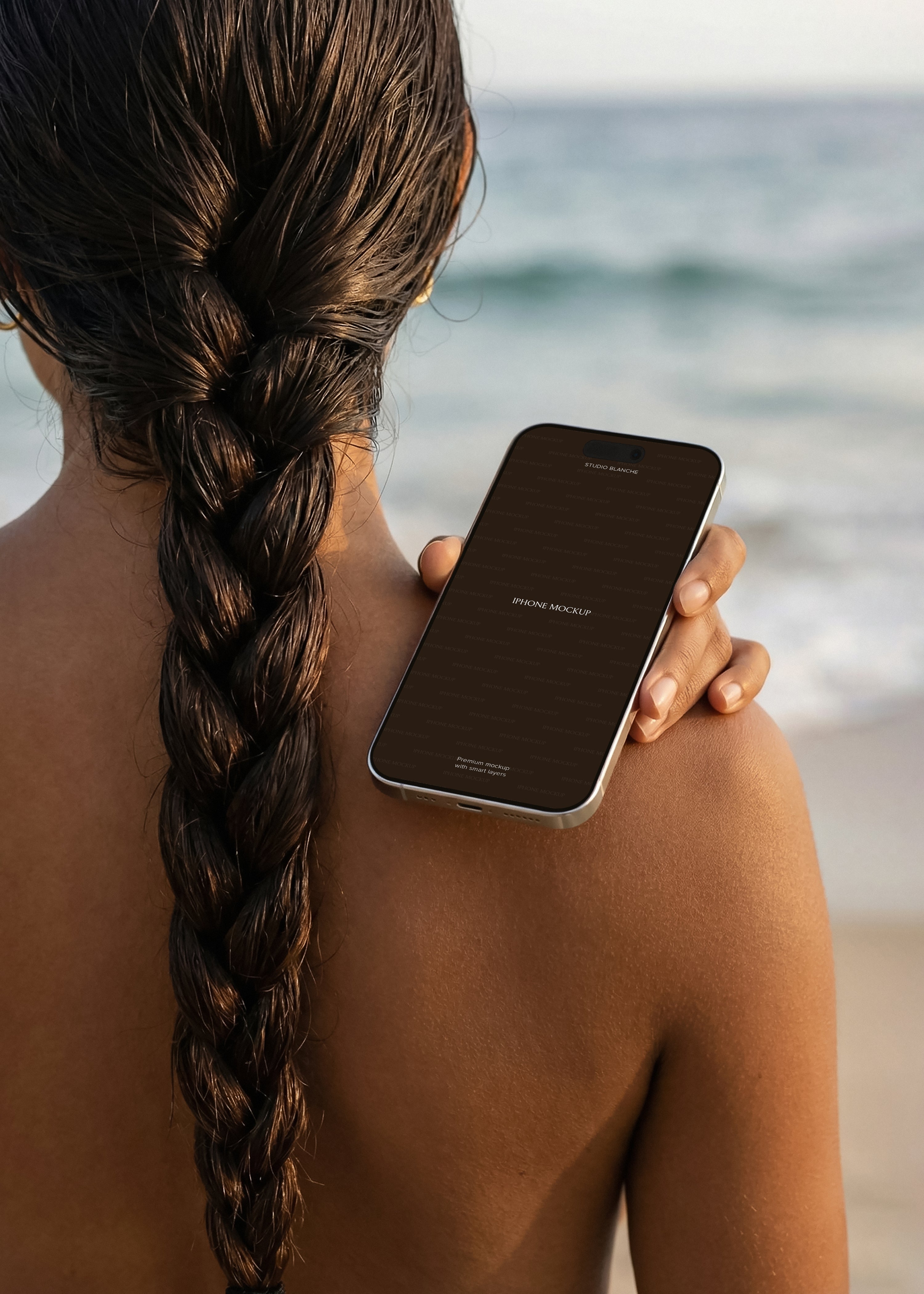 Beach iPhone mockup held against model's bare shoulder, ocean background, warm light, dark screen placeholder