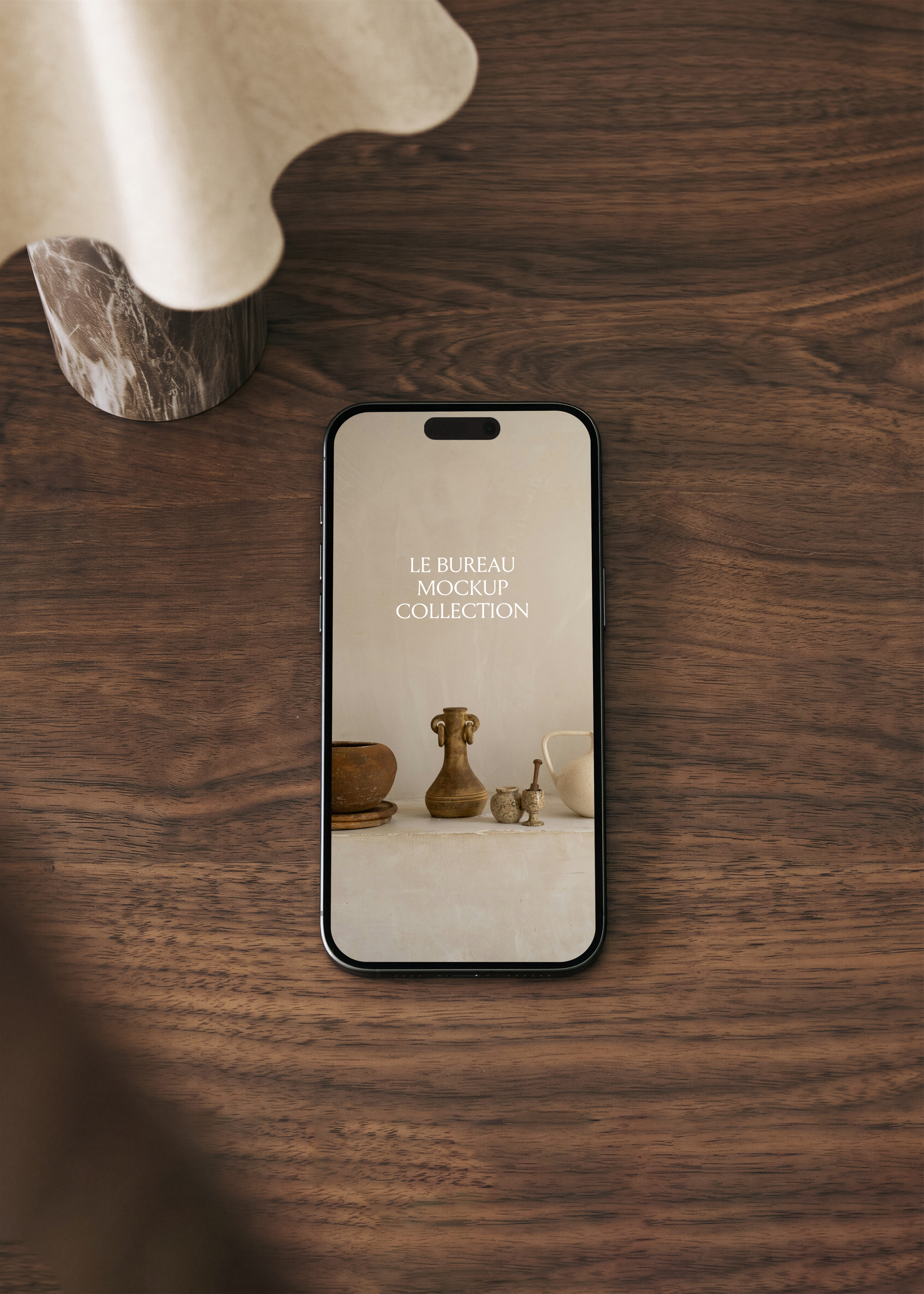 iPhone mockup on walnut surface displaying Le Bureau collection editorial image, dark moody office scene