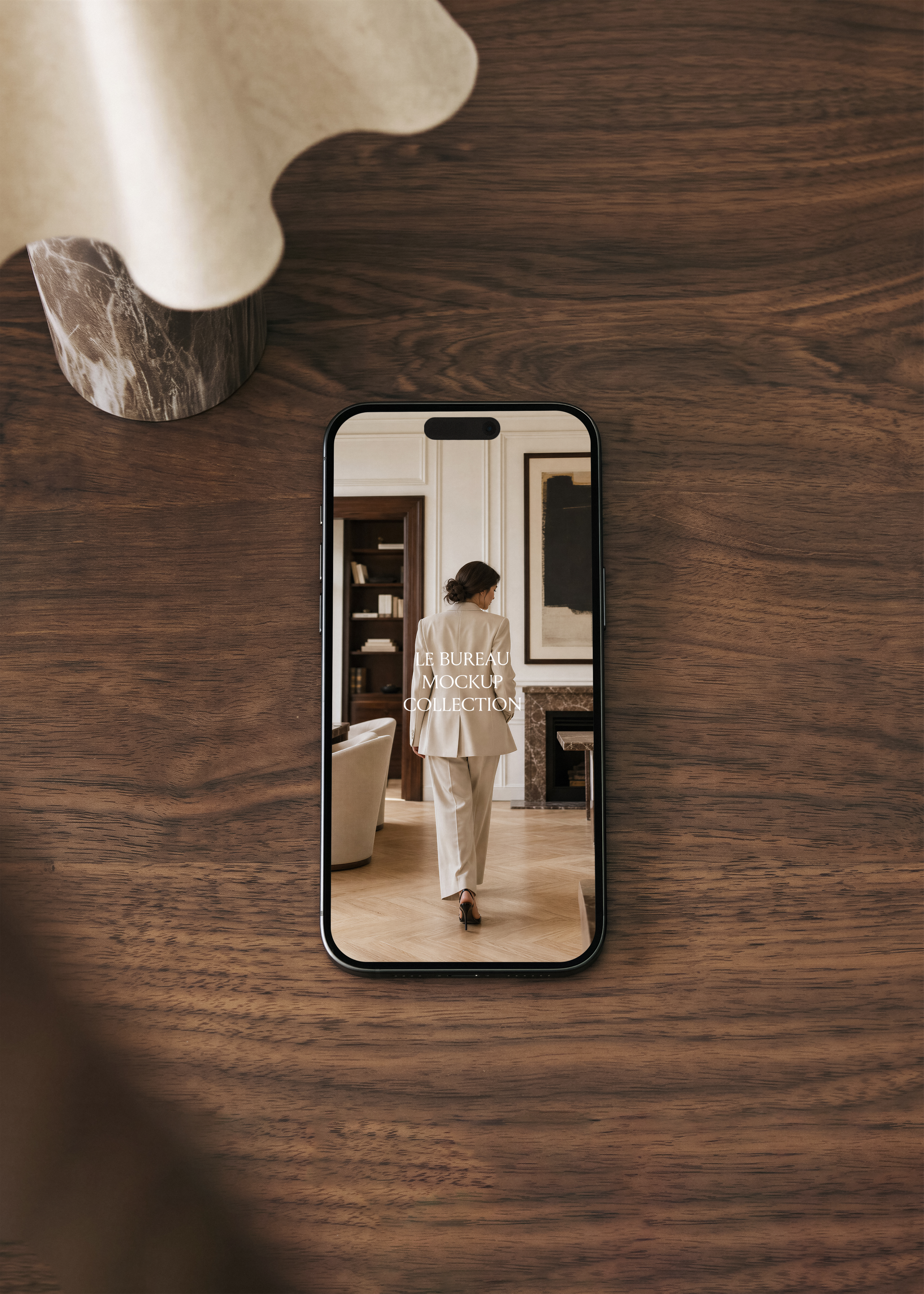 iPhone mockup on walnut surface displaying Le Bureau collection editorial image, dark moody office scene
