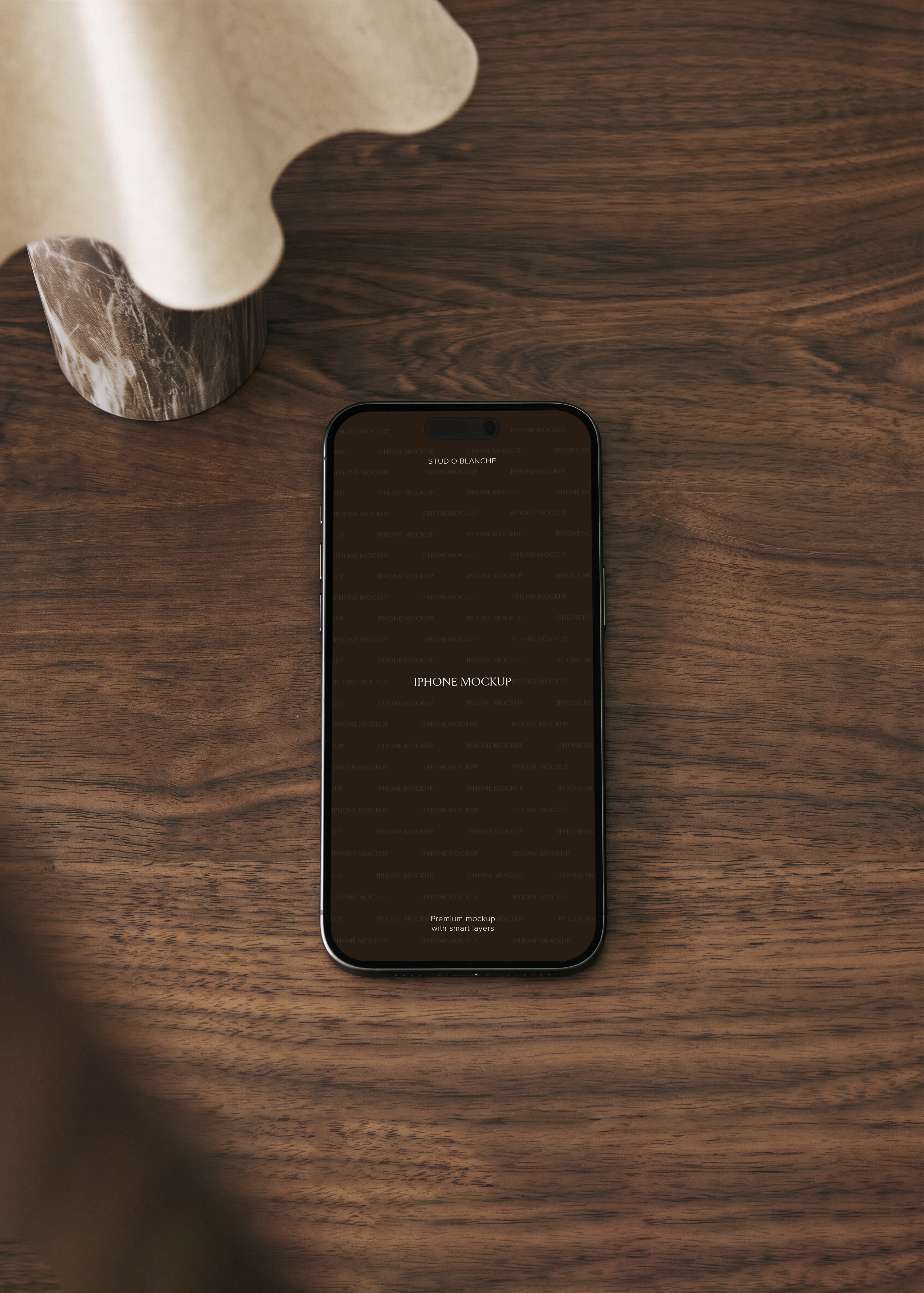 iPhone mockup lying flat on dark walnut wood surface beside sculptural marble ornament, warm brown tones
