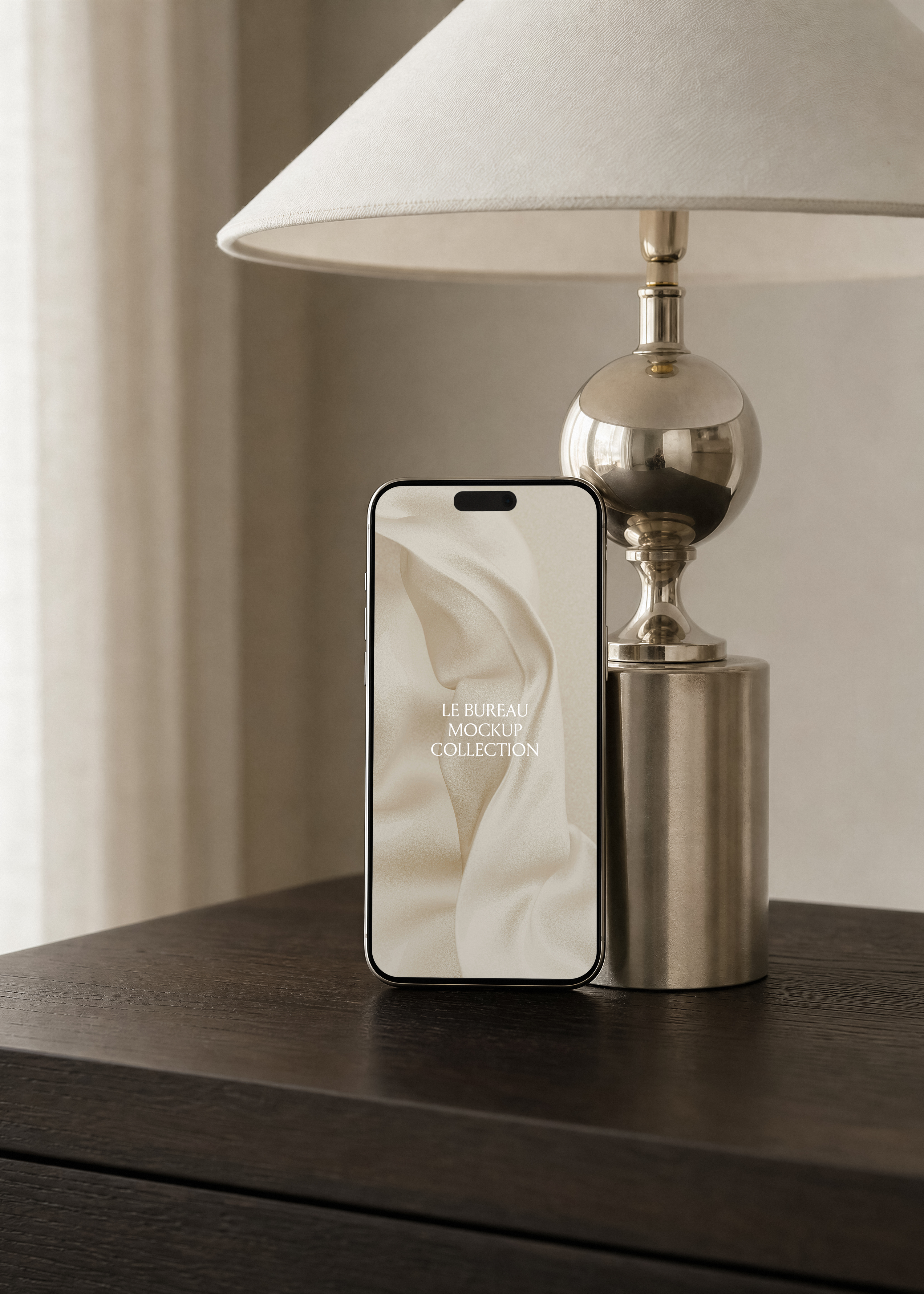 iPhone mockup leaning against polished chrome lamp base on dark oak cabinet, cream lampshade and sheer curtain