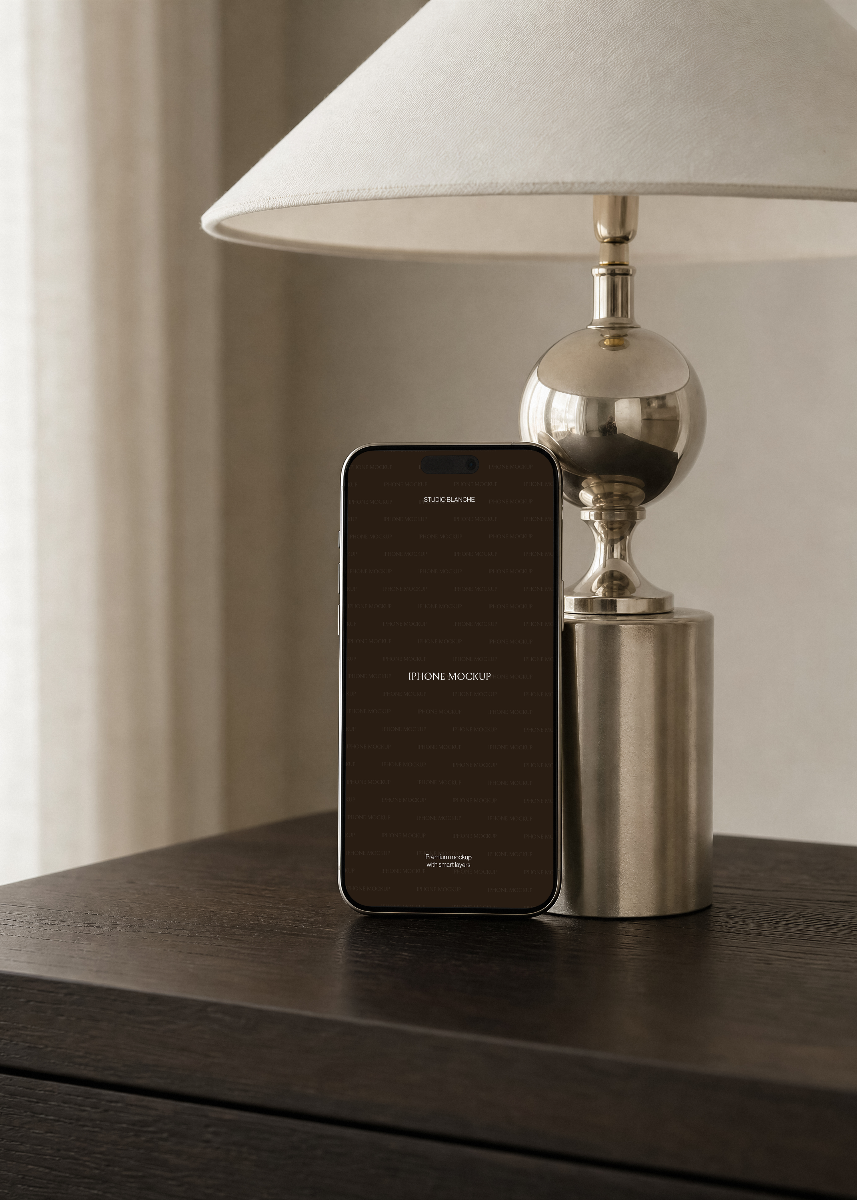 Upright iPhone mockup showing ivory silk image on screen beside chrome ball lamp, warm neutral office interior