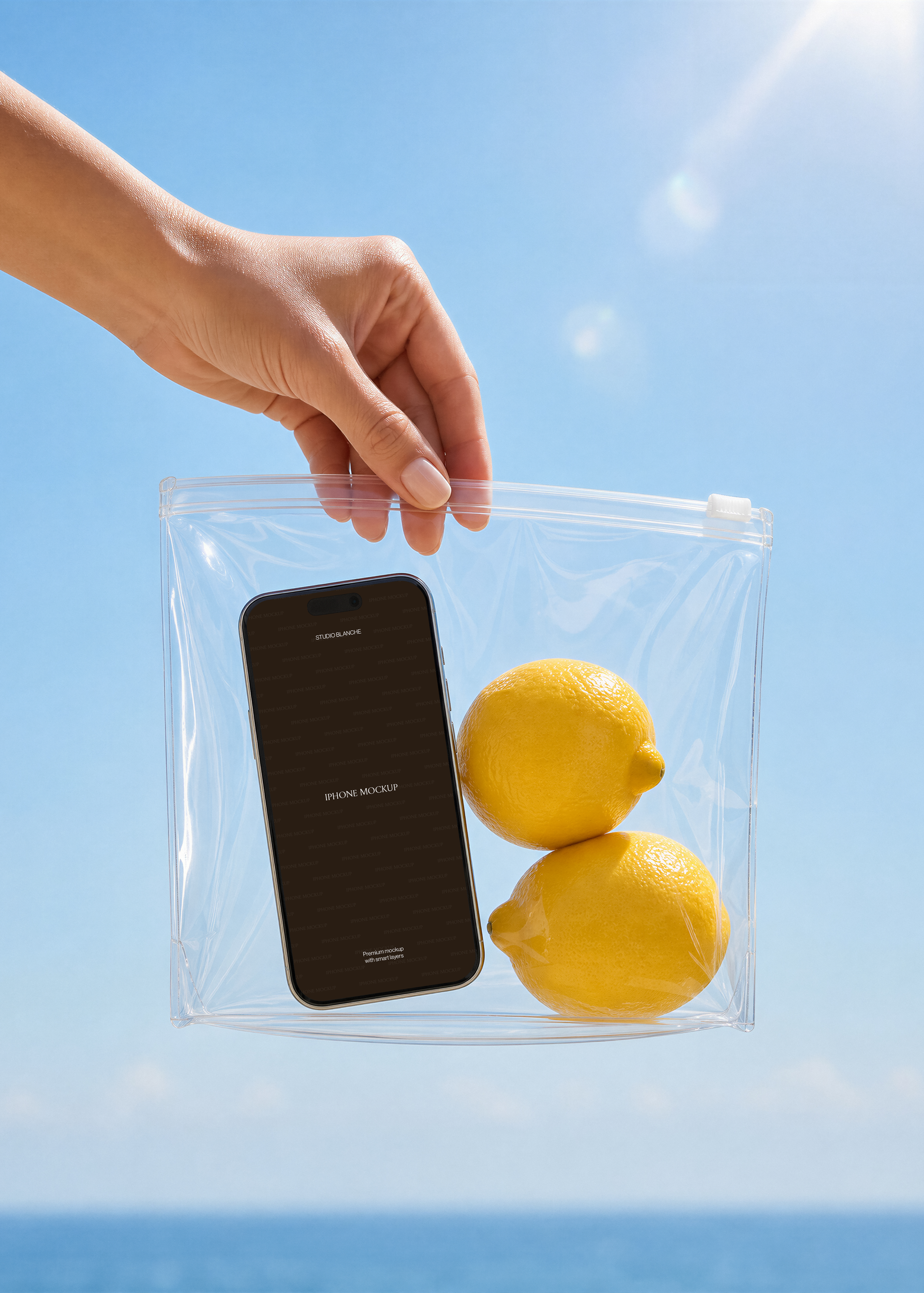 Close view of an iPhone mockup screen beside two yellow lemons in a transparent bag, blue sky and sea, coastal scene