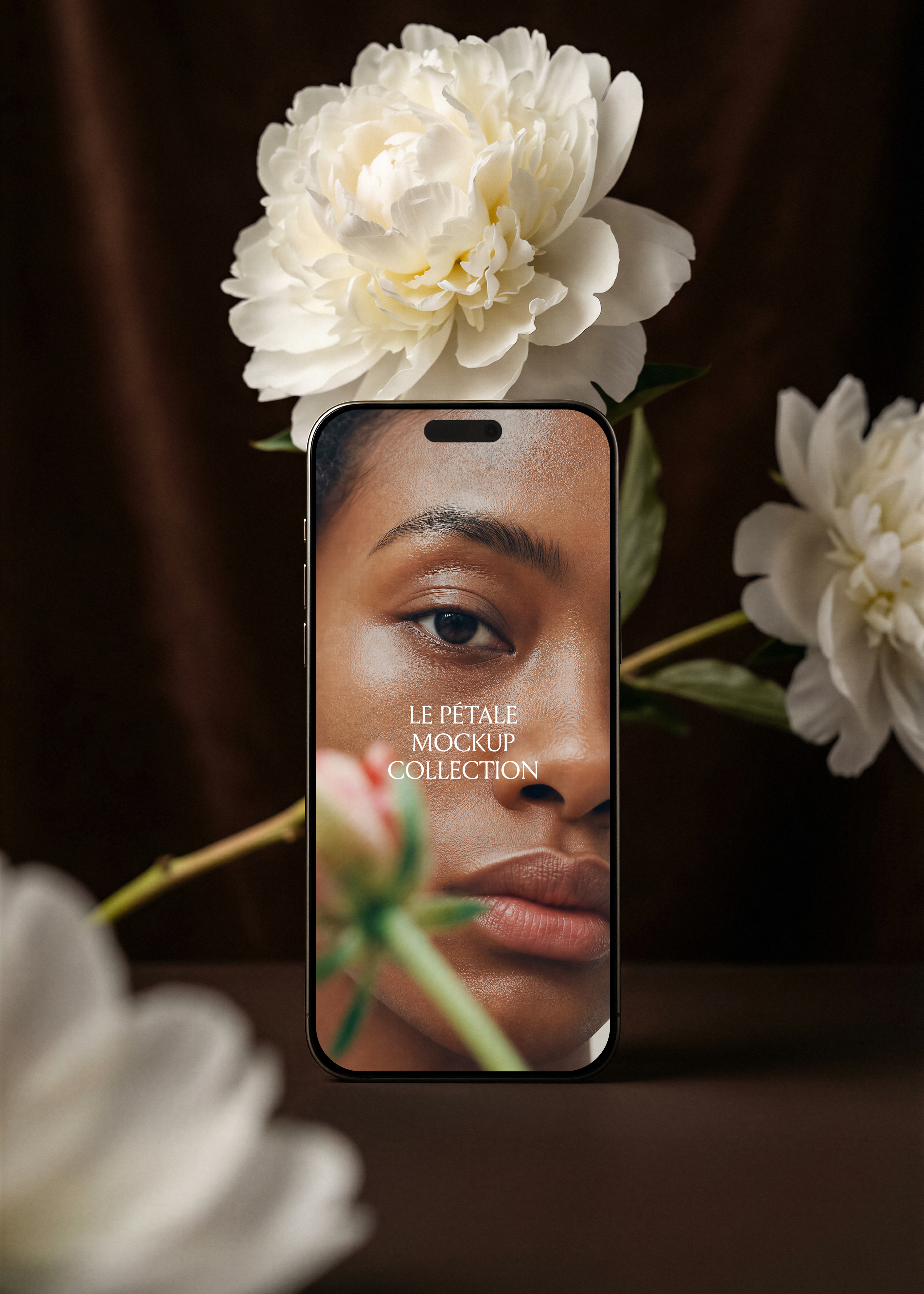 Gold frame iPhone mockup with beauty campaign screen, white peony overhead, blurred peonies left and foreground, dark espresso velvet backdrop