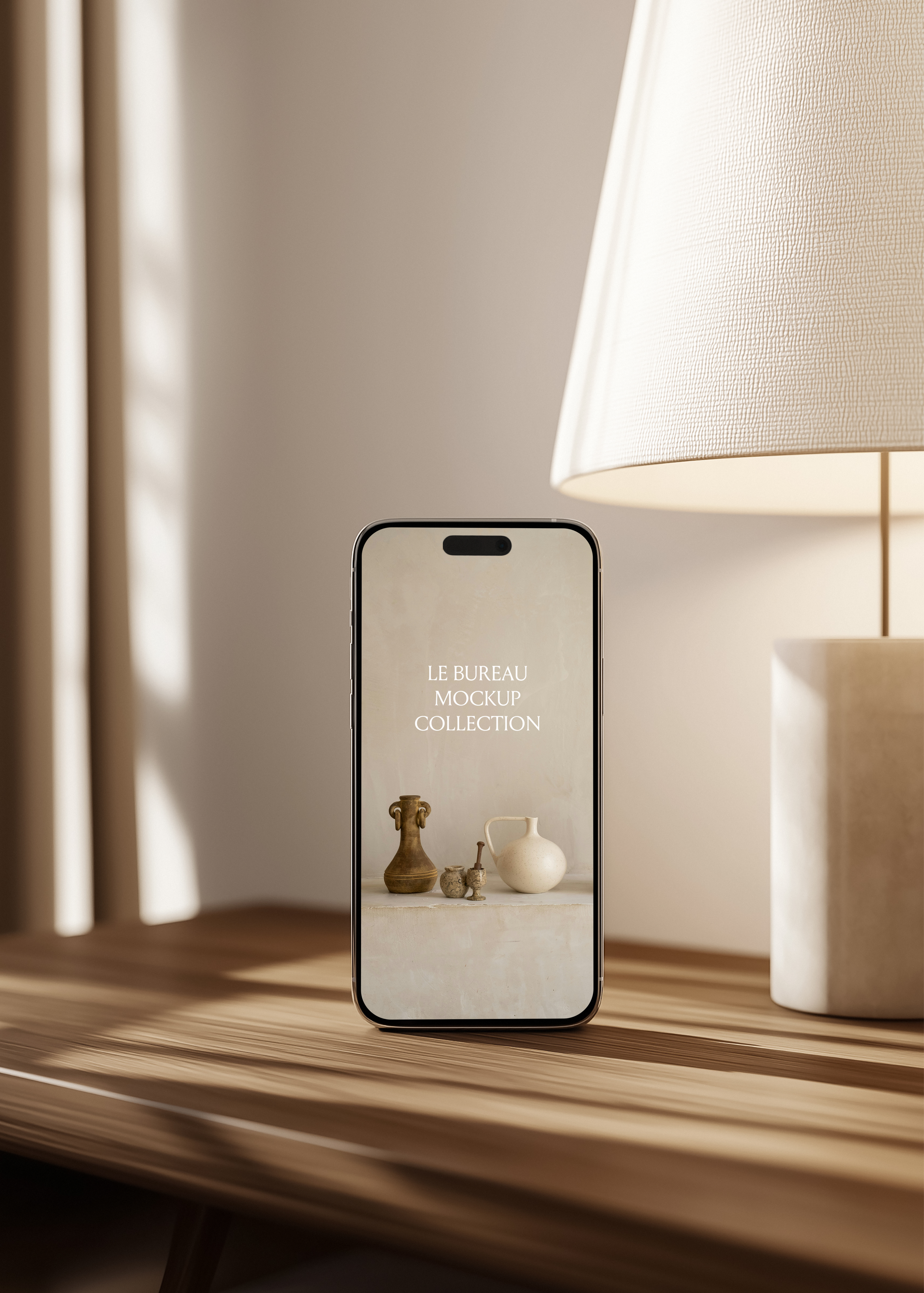 iPhone mockup displaying Le Bureau editorial on oak surface, stone lamp with linen shade and warm dappled wall light