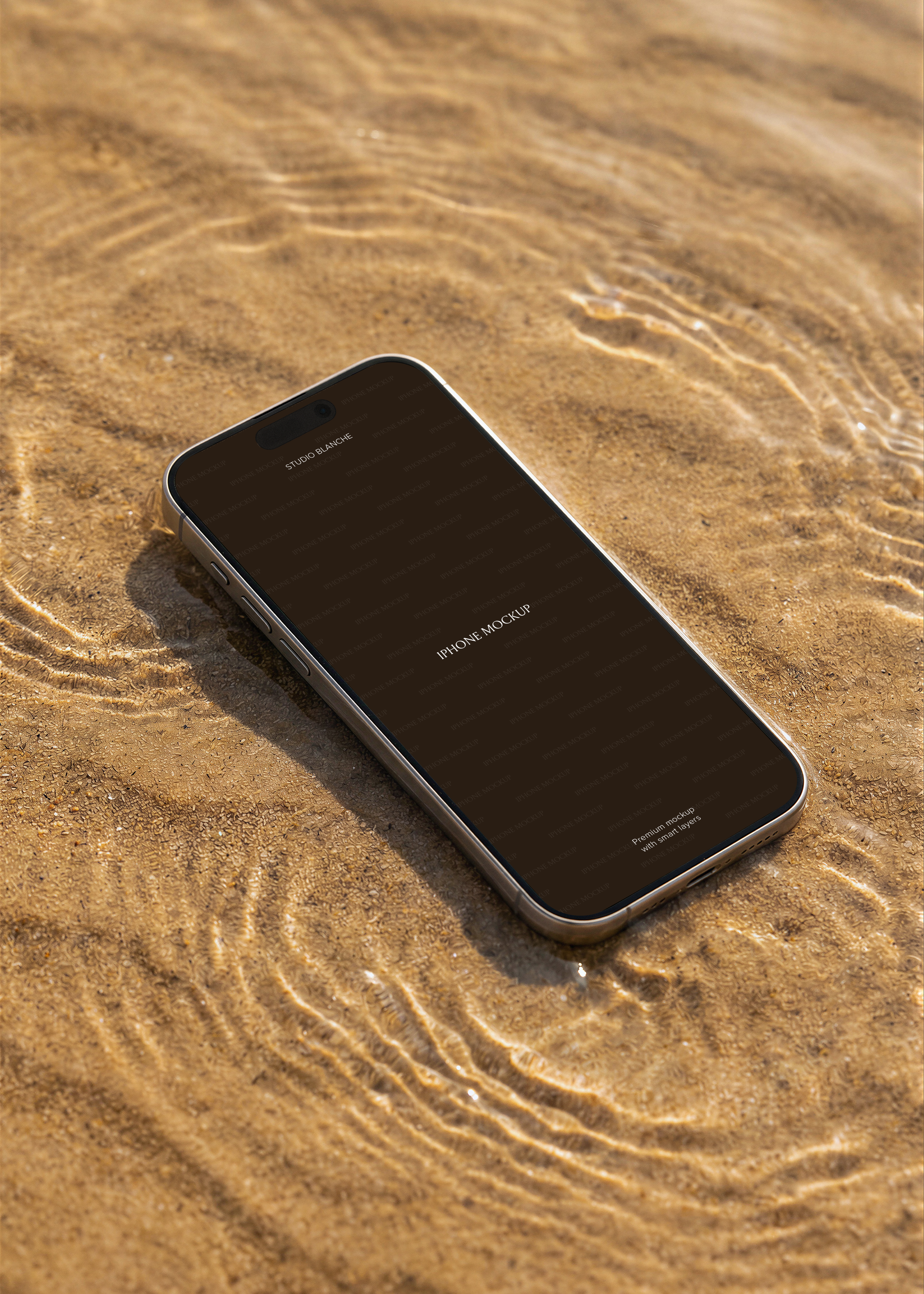 Beach iPhone mockup on golden sand with water ripples, dark screen placeholder, warm editorial styling