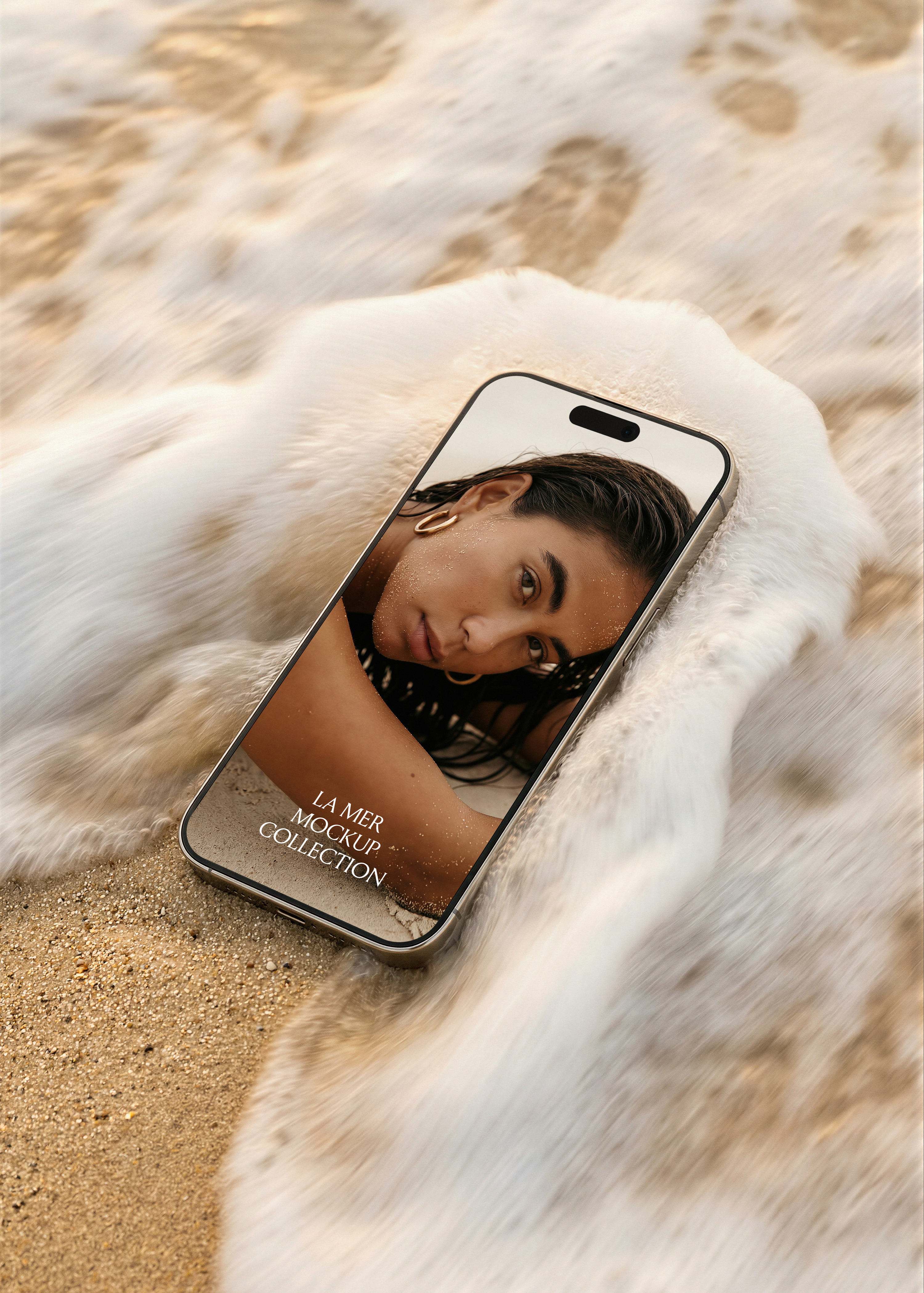 iPhone mockup on wet sand surrounded by soft-focus breaking wave, editorial beauty campaign example screen