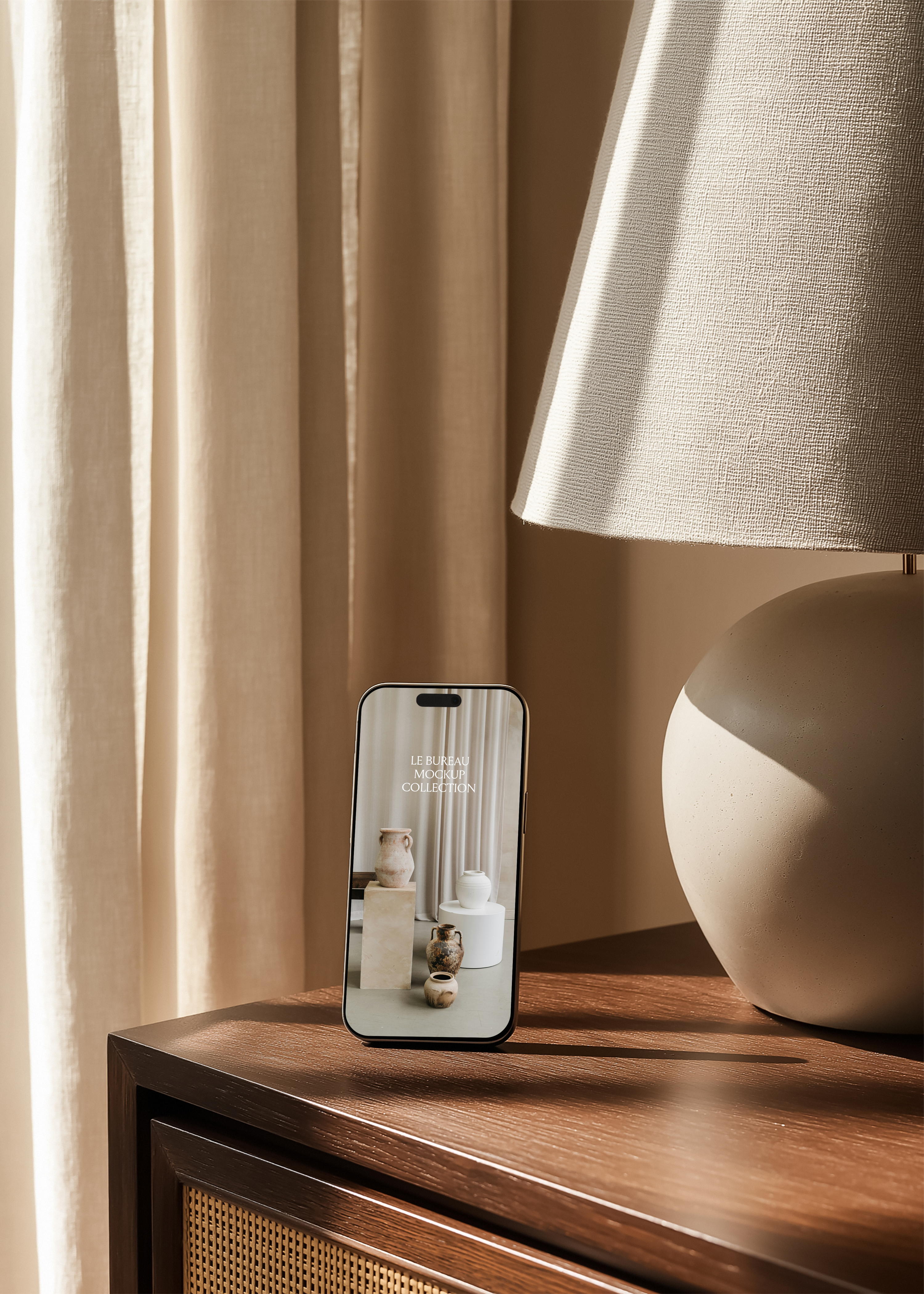 iPhone mockup displaying Le Bureau editorial on dark oak rattan cabinet, clay sphere lamp and floor-length linen curtains