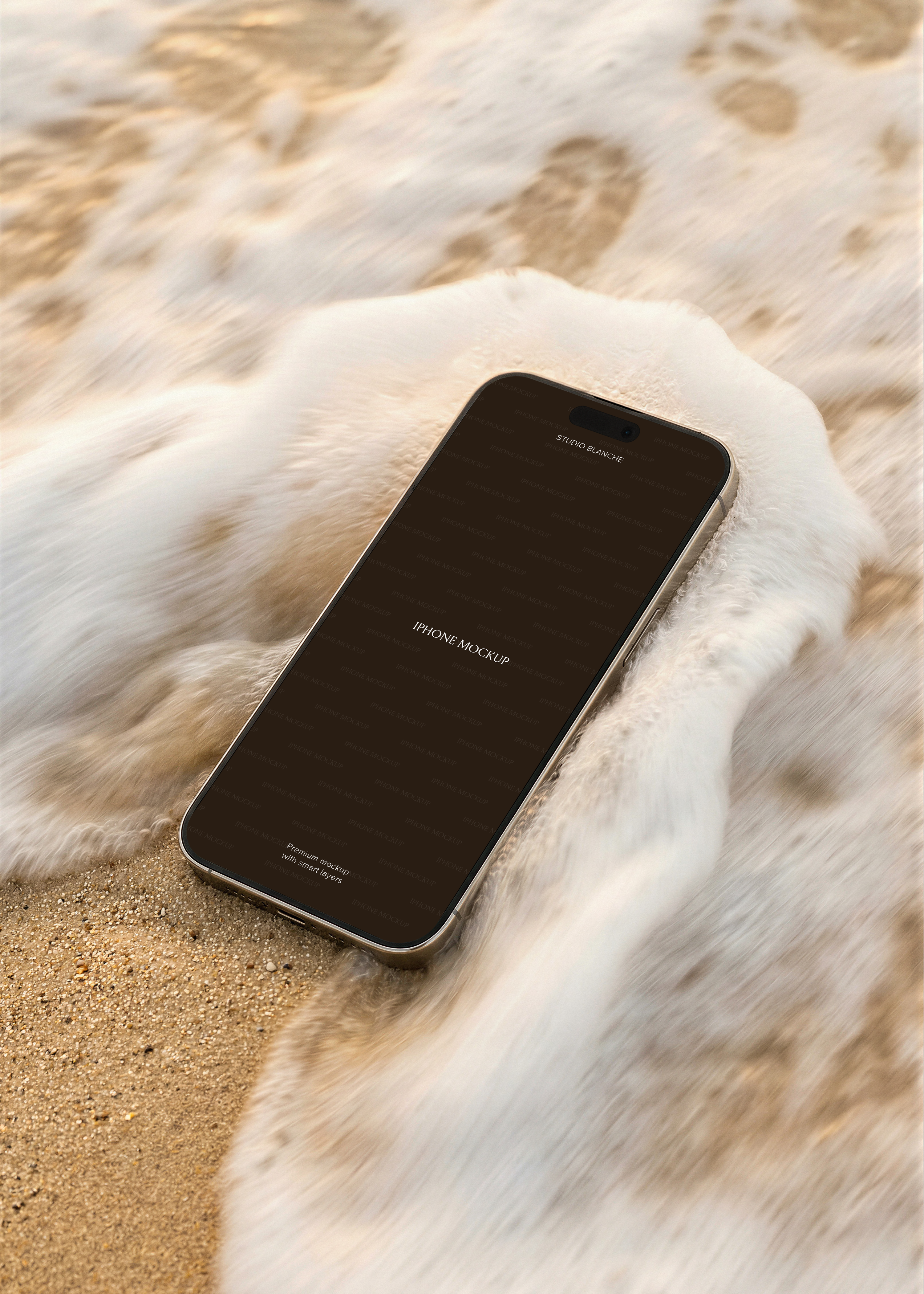 iPhone lying flat on sandy beach with motion-blurred wave rushing past, warm golden sand, angled perspective