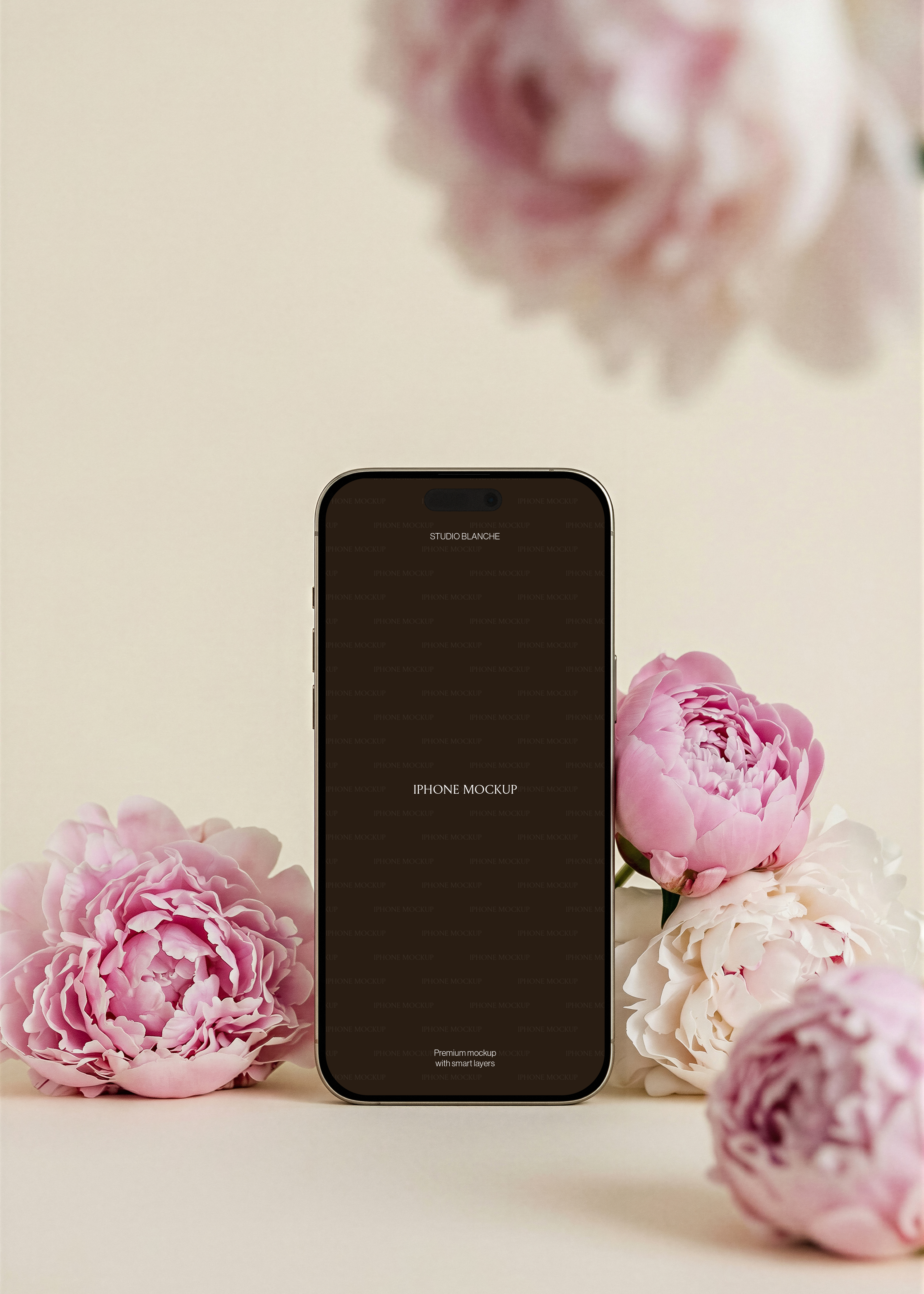Gold iPhone mockup with screen area, mixed pink peonies surrounding base, blurred peony bloom overhead, beige background