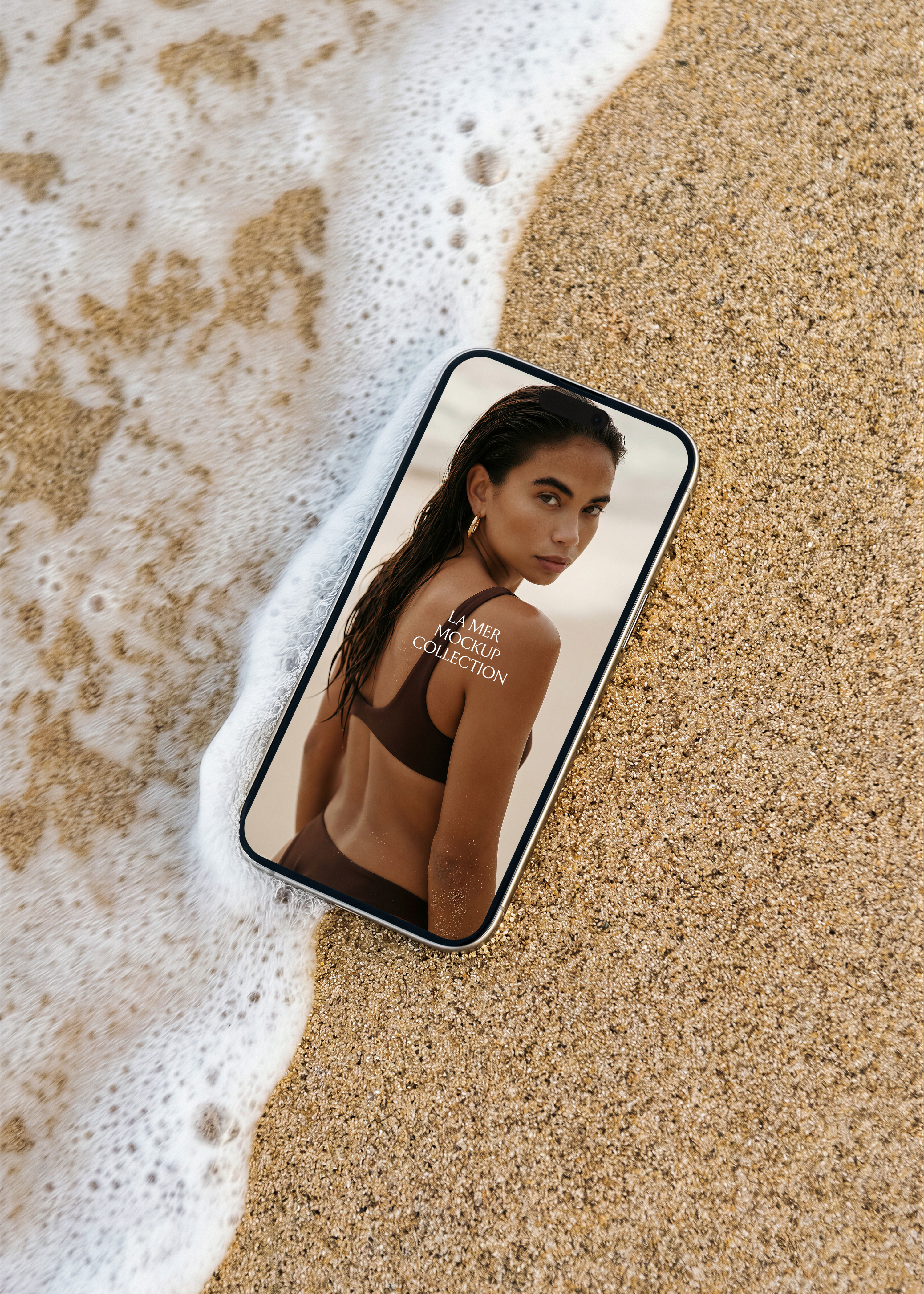 iPhone mockup on sandy beach beside retreating wave foam, editorial swimwear campaign image on screen