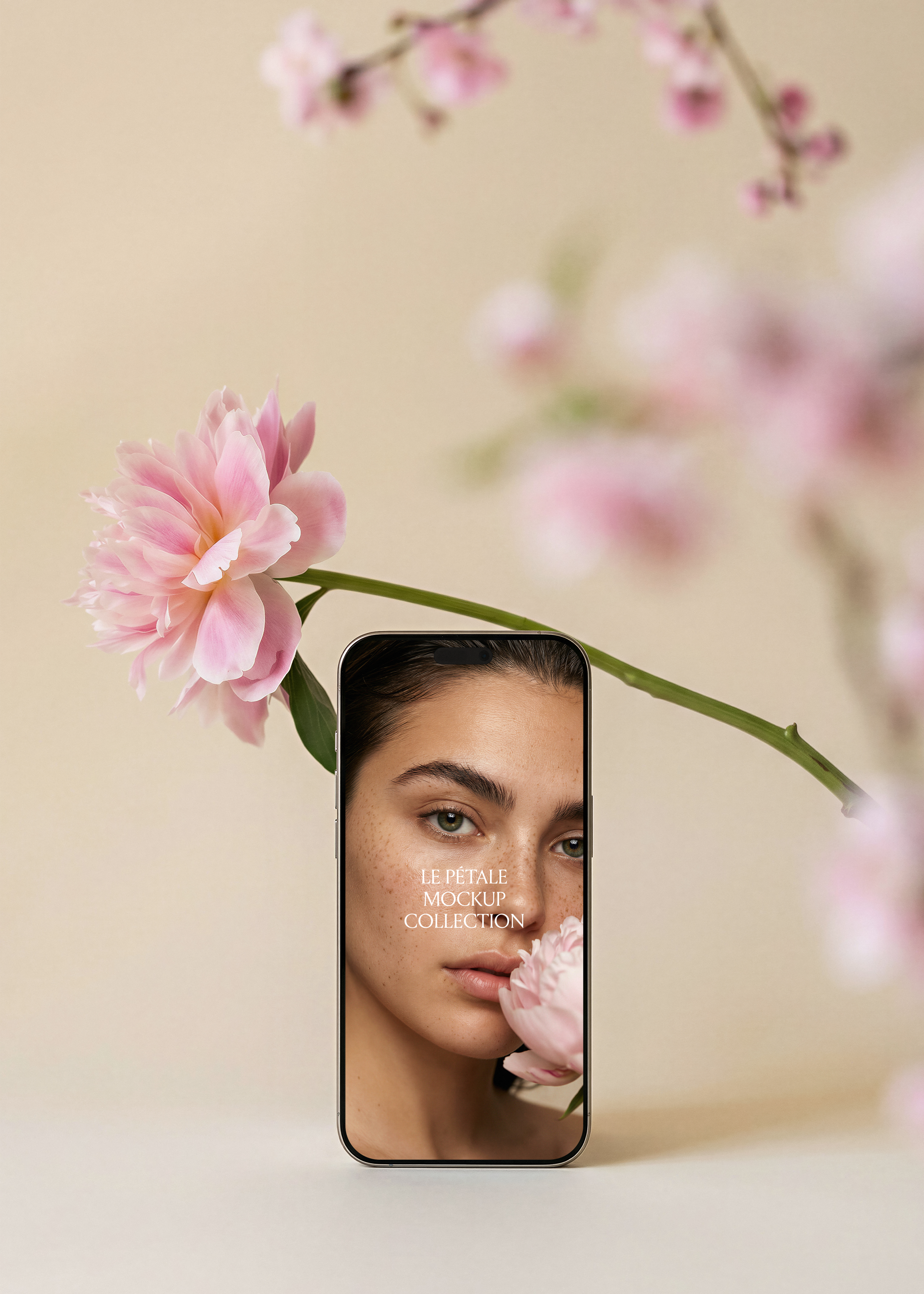 Gold frame iPhone mockup with beauty campaign screen, pink peony stem arcing left, blurred cherry blossom branches background, sand backdrop