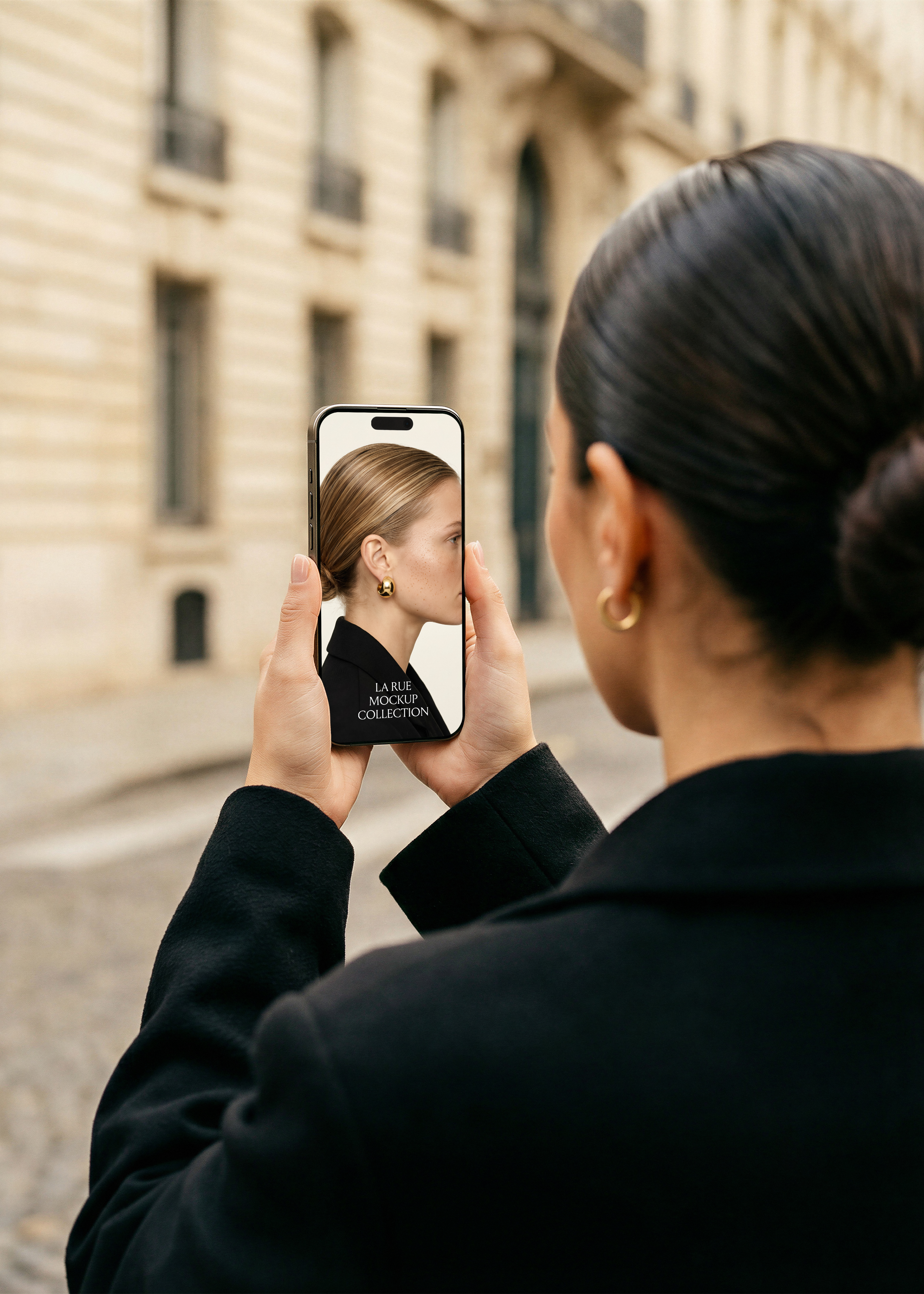 Woman in black holding iPhone with both hands on Paris cobblestone street, screen showing editorial fashion website
