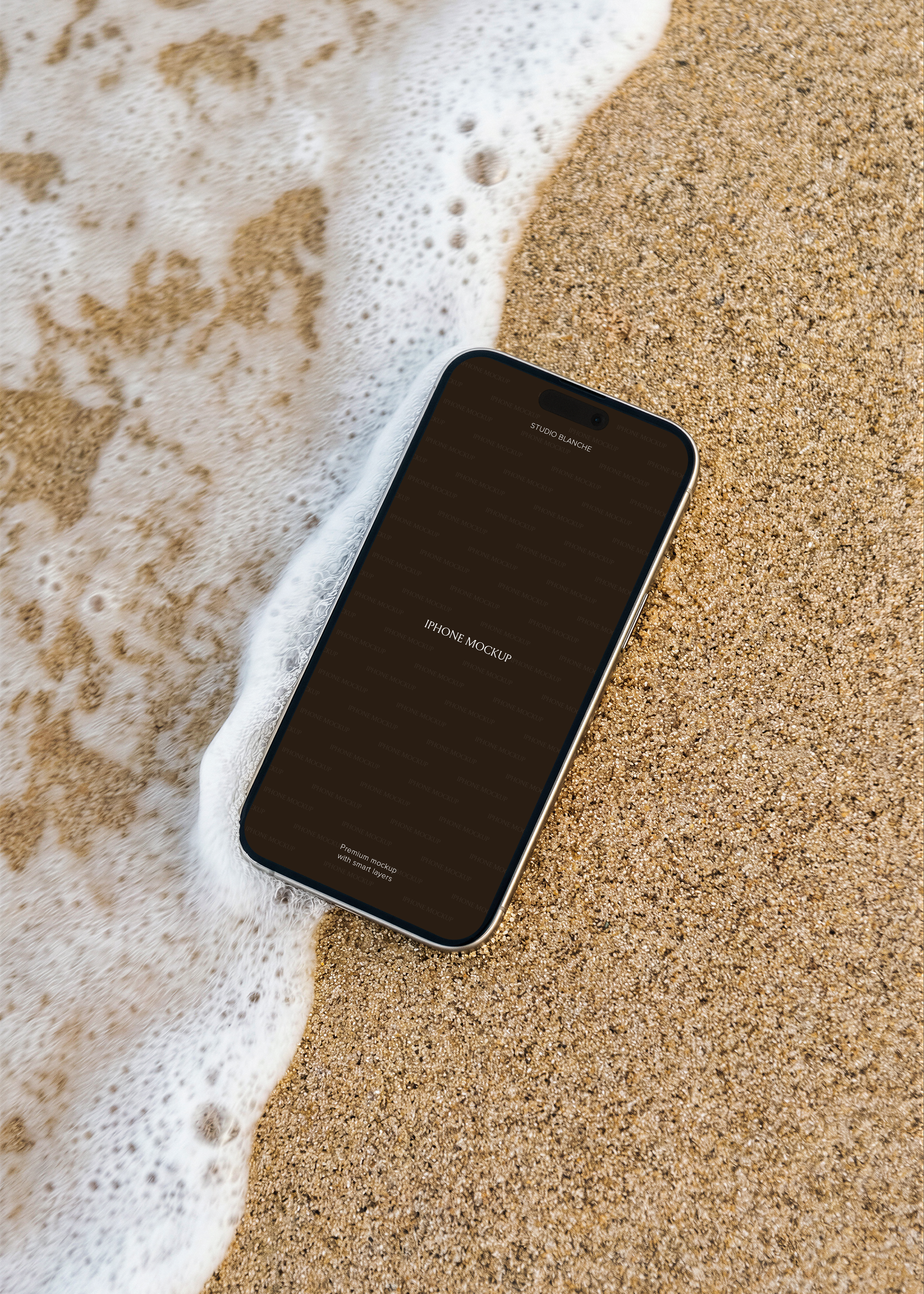 iPhone lying flat on coarse golden sand at shoreline with foaming wave edge, overhead perspective, coastal mockup