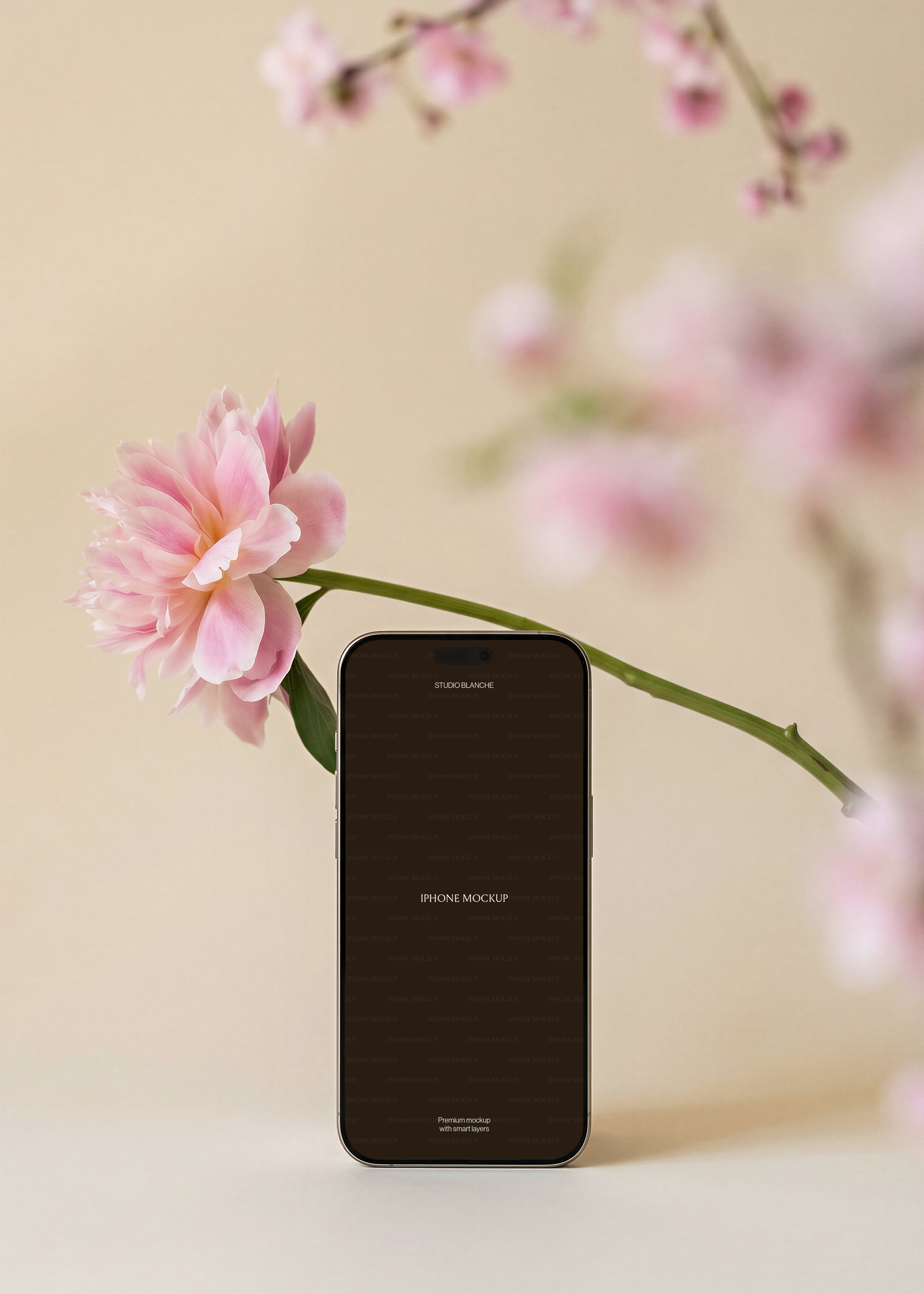 iPhone mockup with screen area, diagonal pink peony stem from left, blurred cherry blossom branches background, warm beige surface