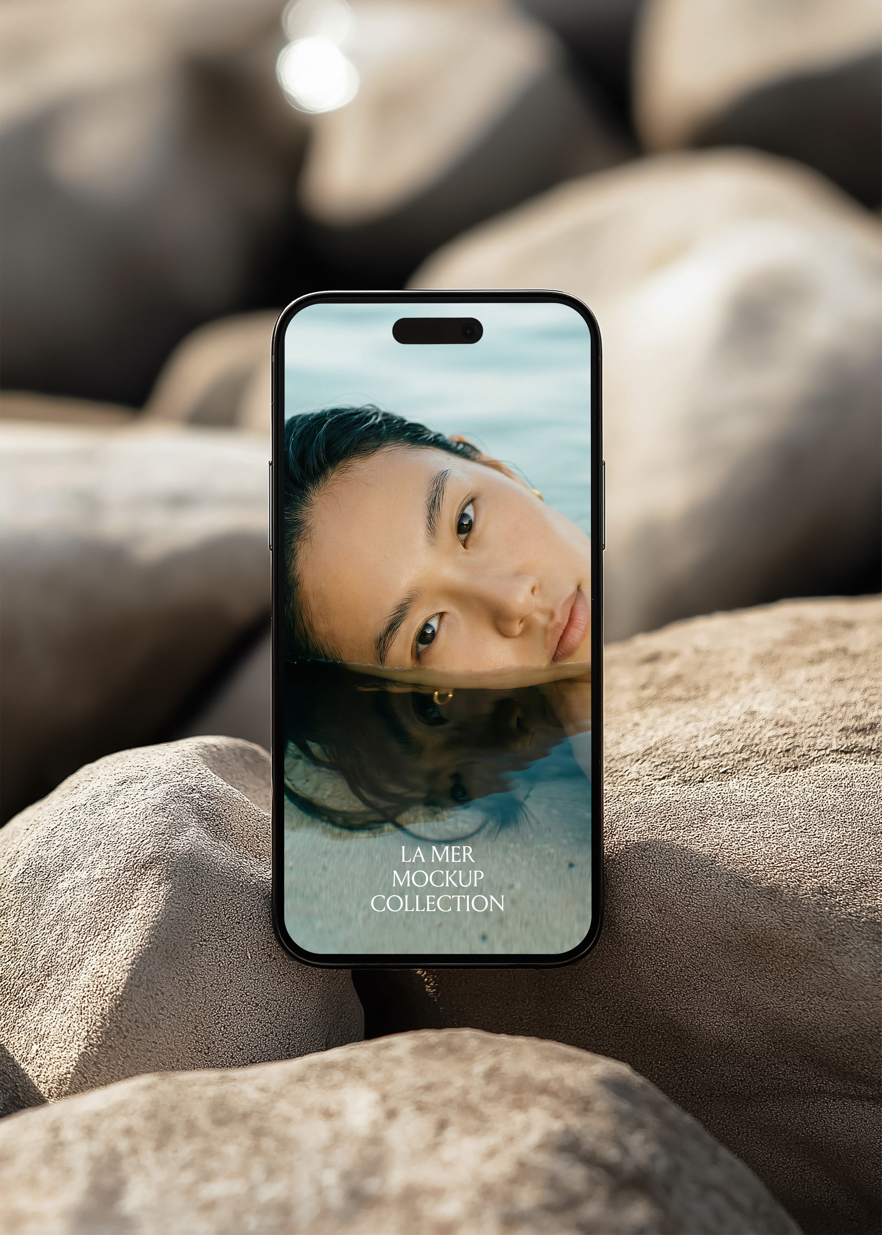 iPhone mockup propped on textured coastal rocks, editorial beauty campaign image on screen, shallow depth of field