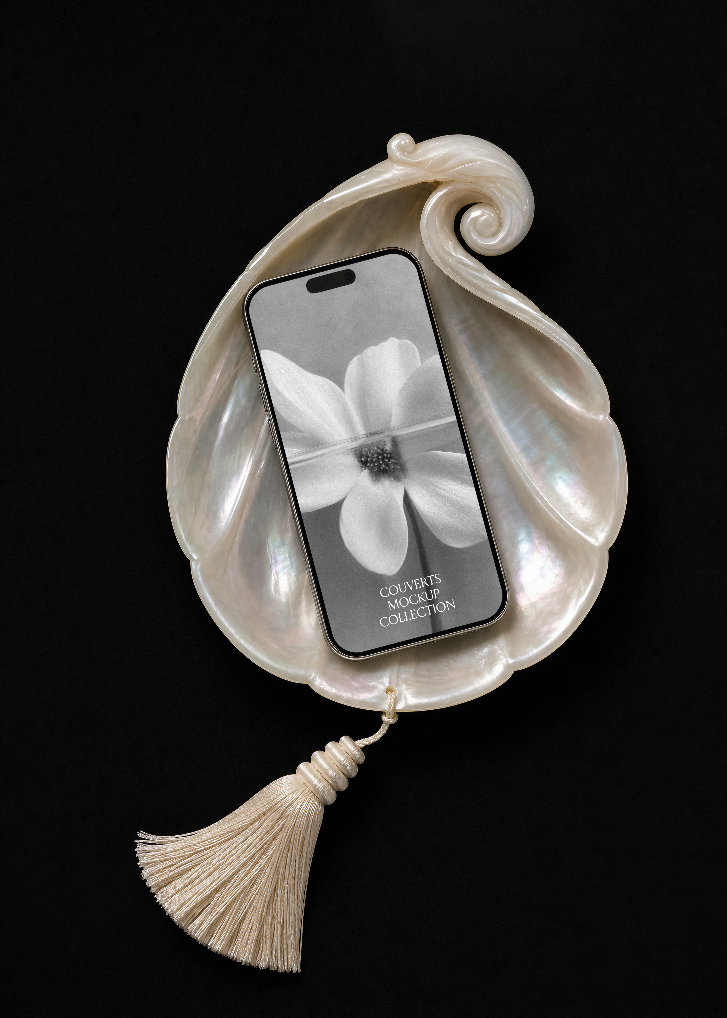 iPhone mockup resting in an iridescent mother of pearl shell dish with cream silk tassel on black background, flat lay