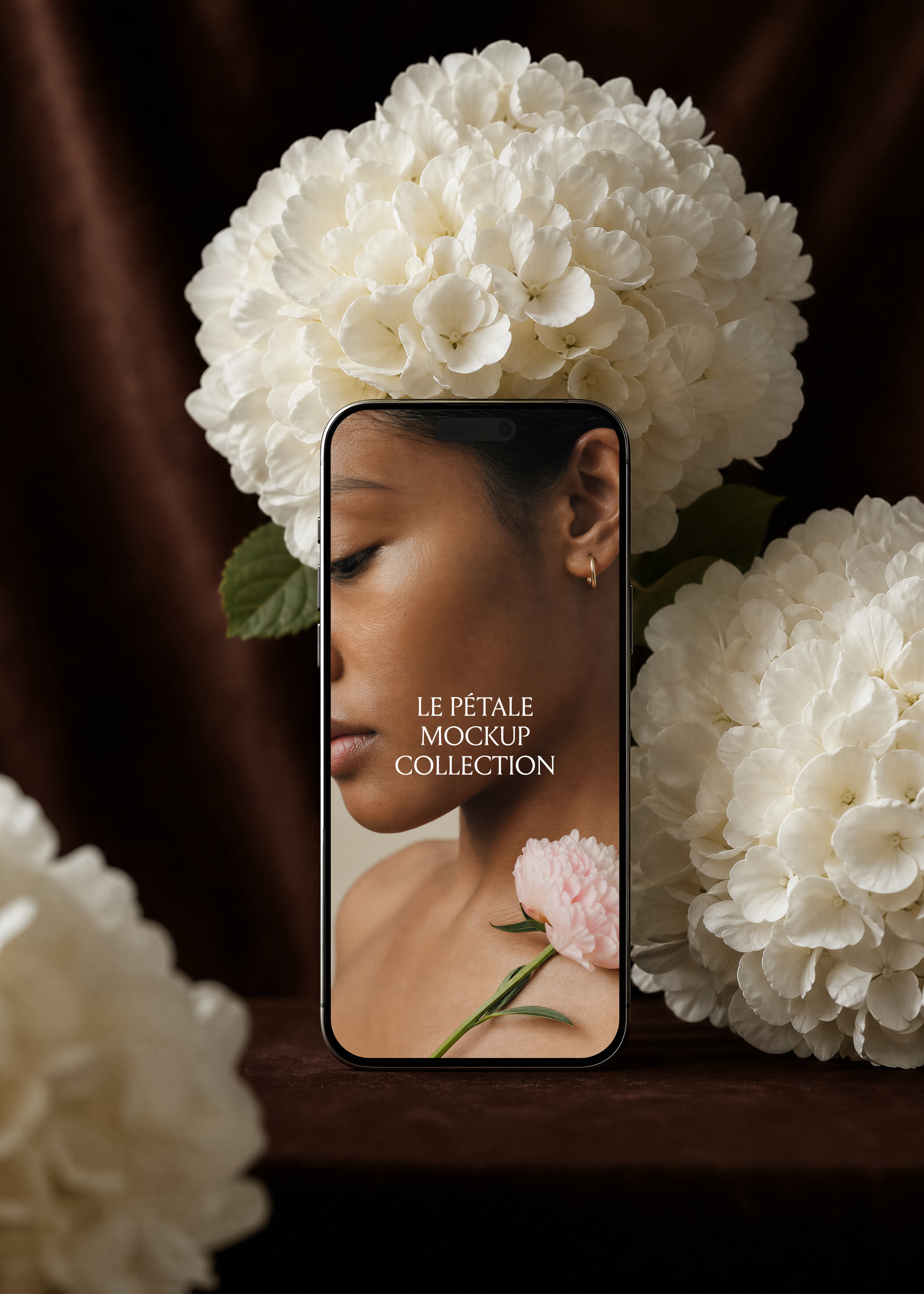 iPhone mockup with portrait screen design propped against white hydrangea blooms and dark velvet, peony resting at collarbone