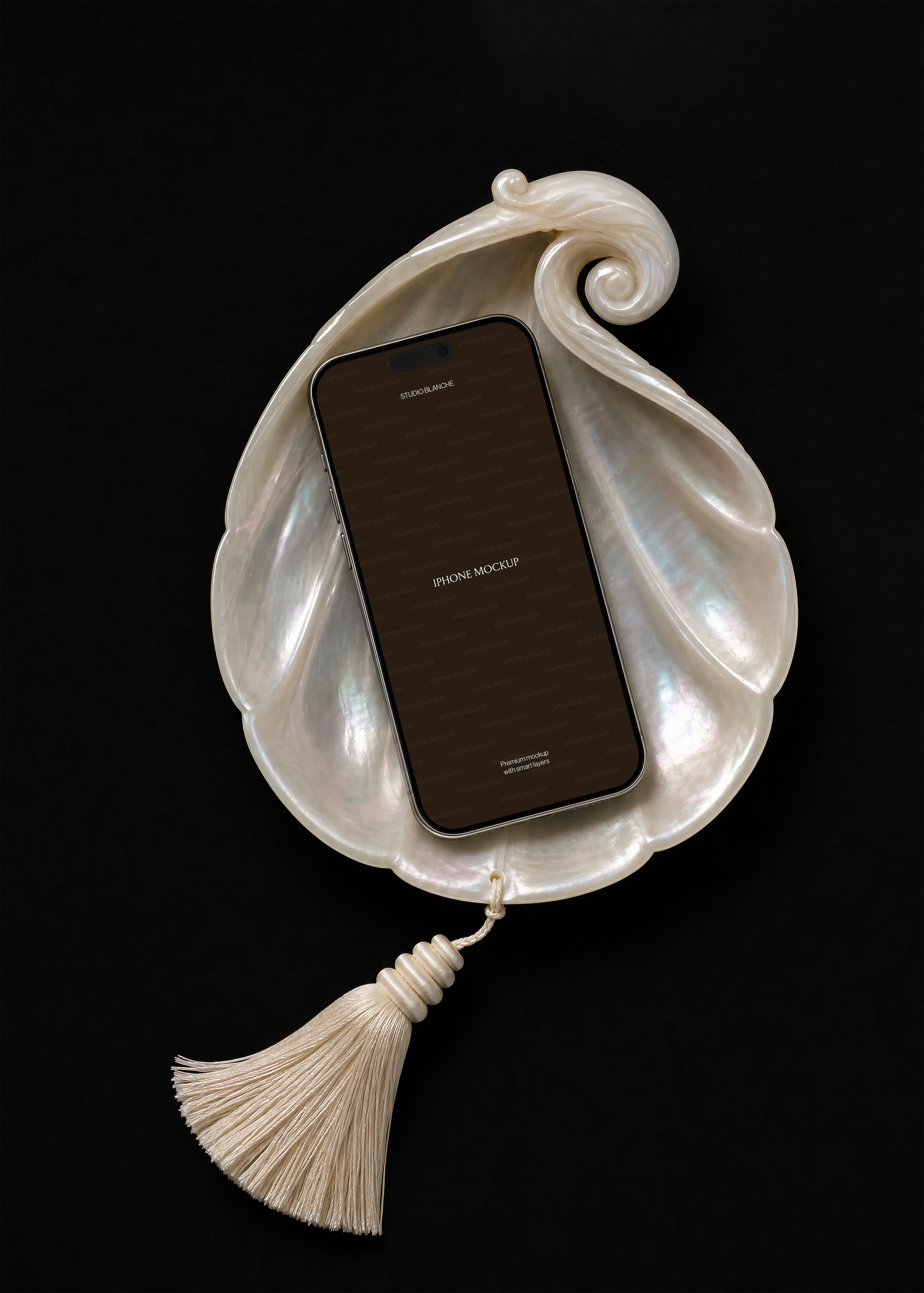 iPhone mockup with dark screen in pearl shell tray, cream tassel below, black backdrop, close crop showing nacre sheen