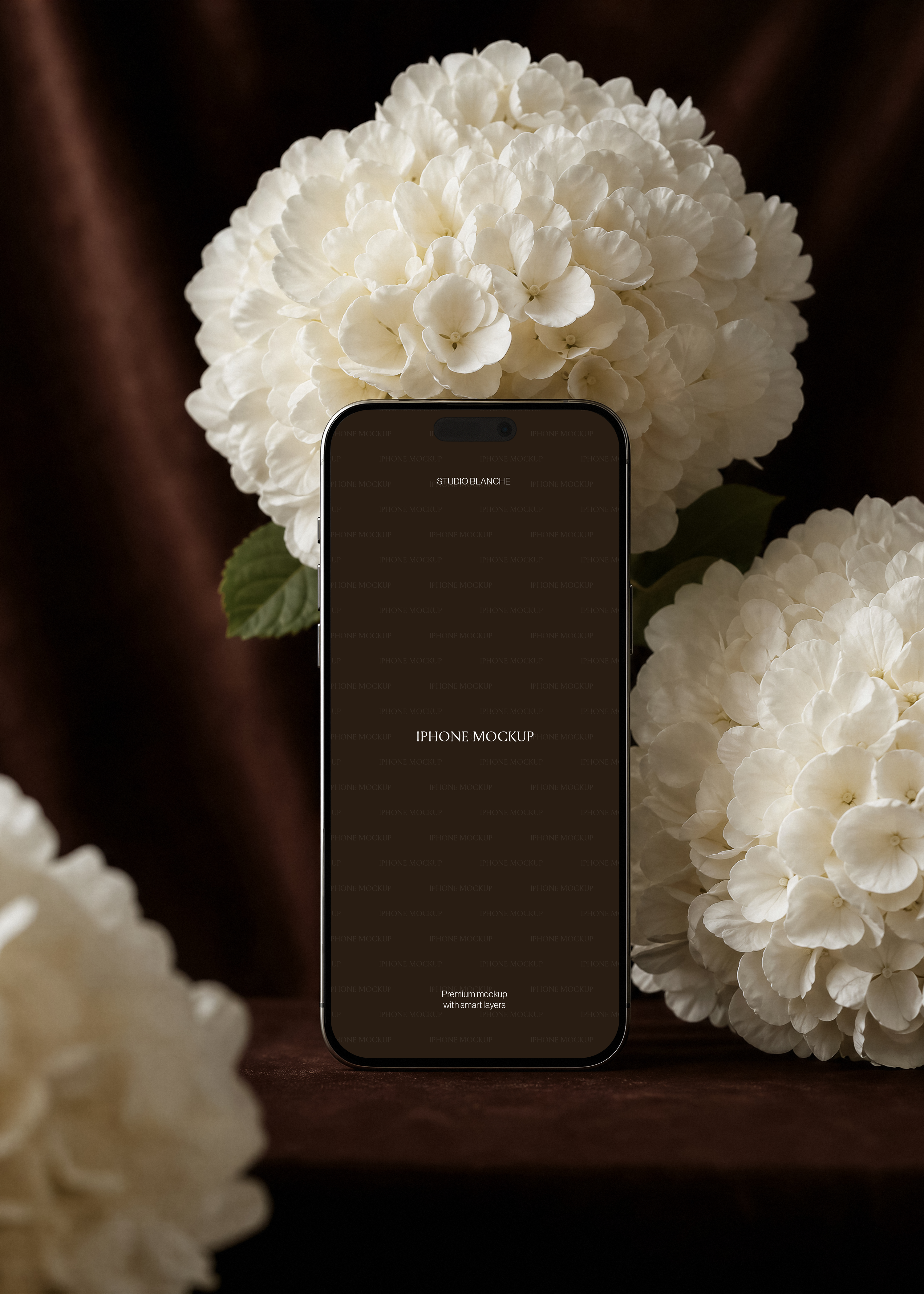iPhone mockup with plain text screen design beside white hydrangea blooms on dark velvet, editorial floral styling