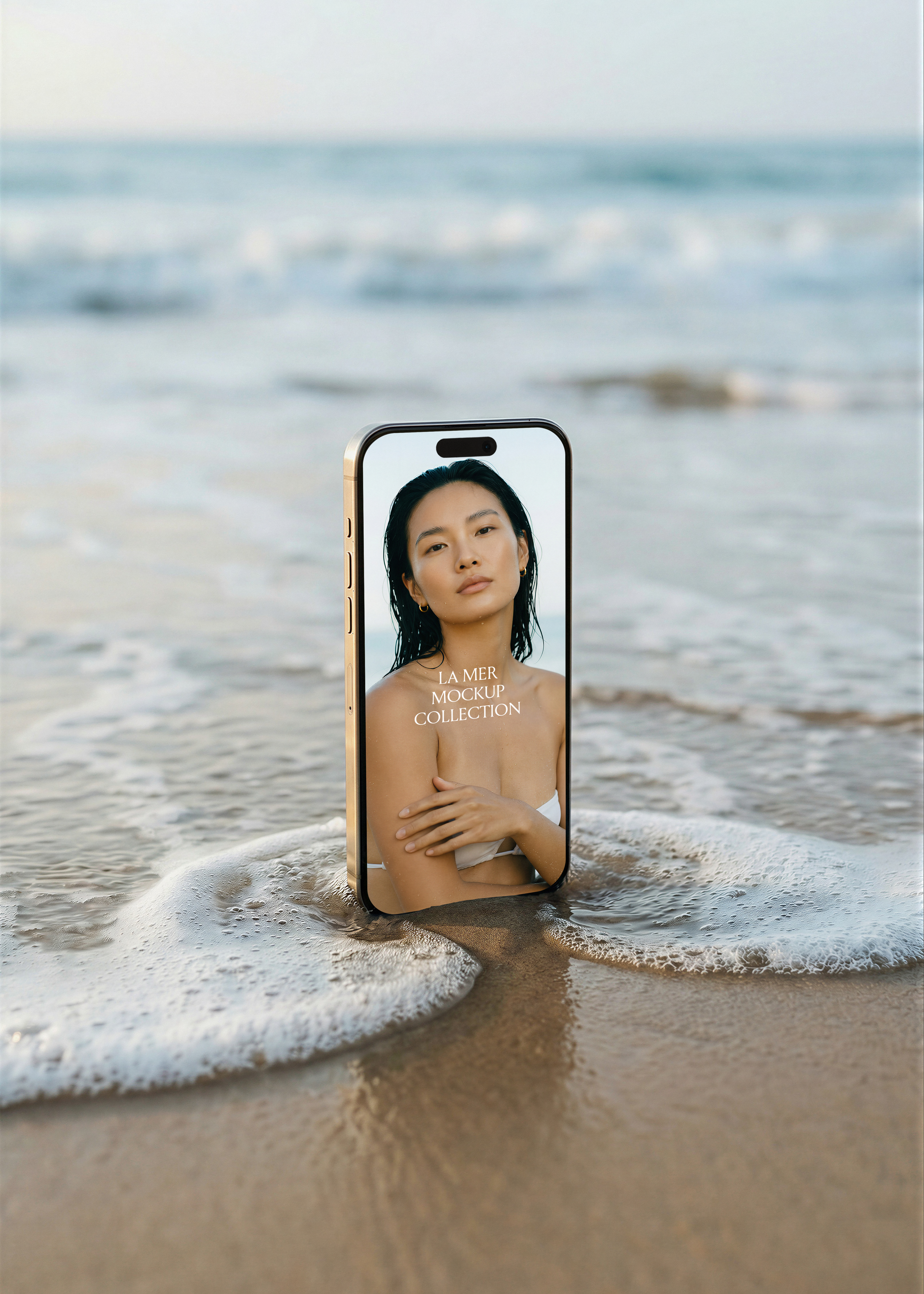 iPhone mockup in shoreline wave with blue sky horizon, editorial beauty campaign image on screen, gold frame