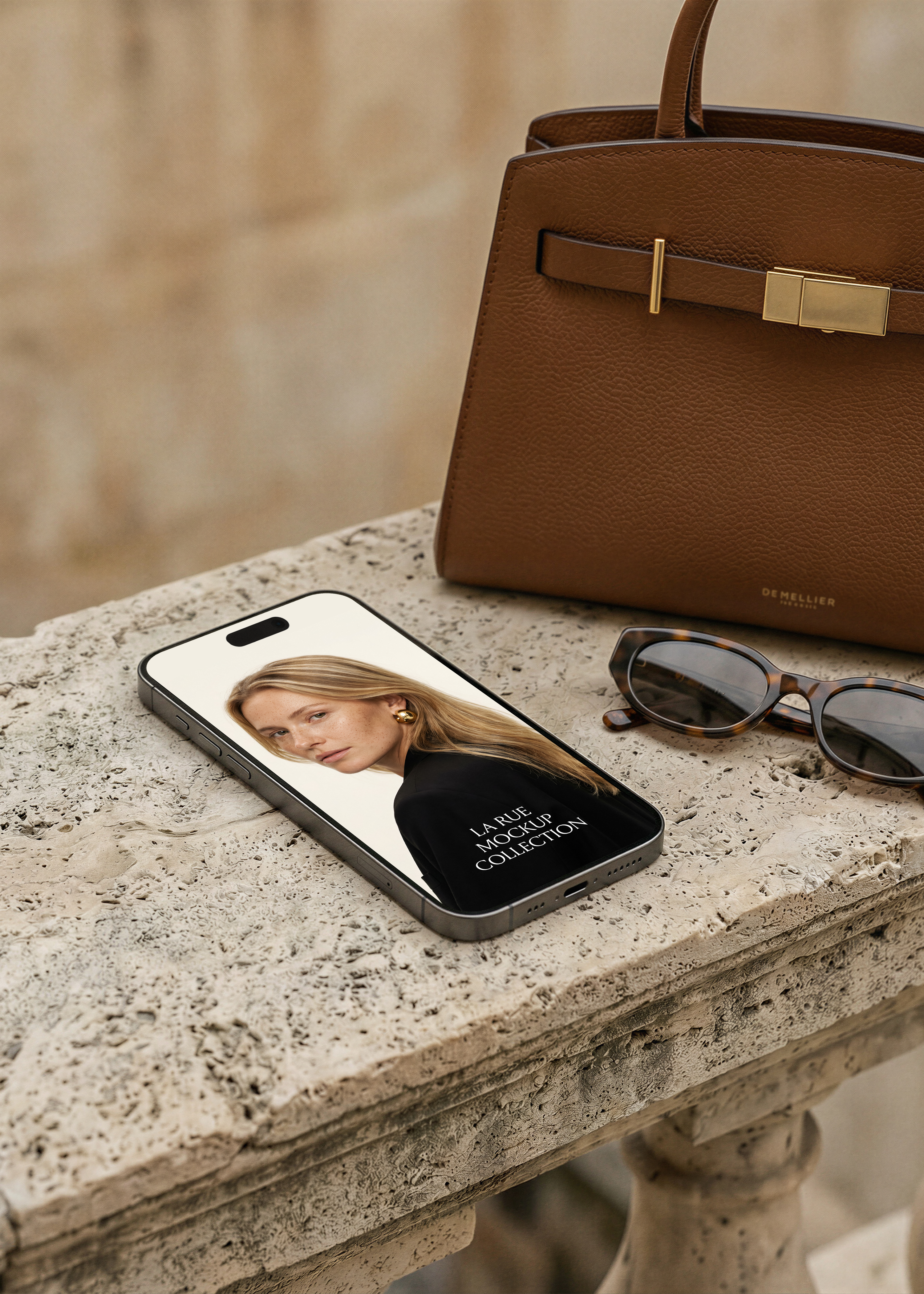 iPhone on weathered stone ledge beside tan structured leather bag and tortoiseshell sunglasses, editorial fashion website on screen