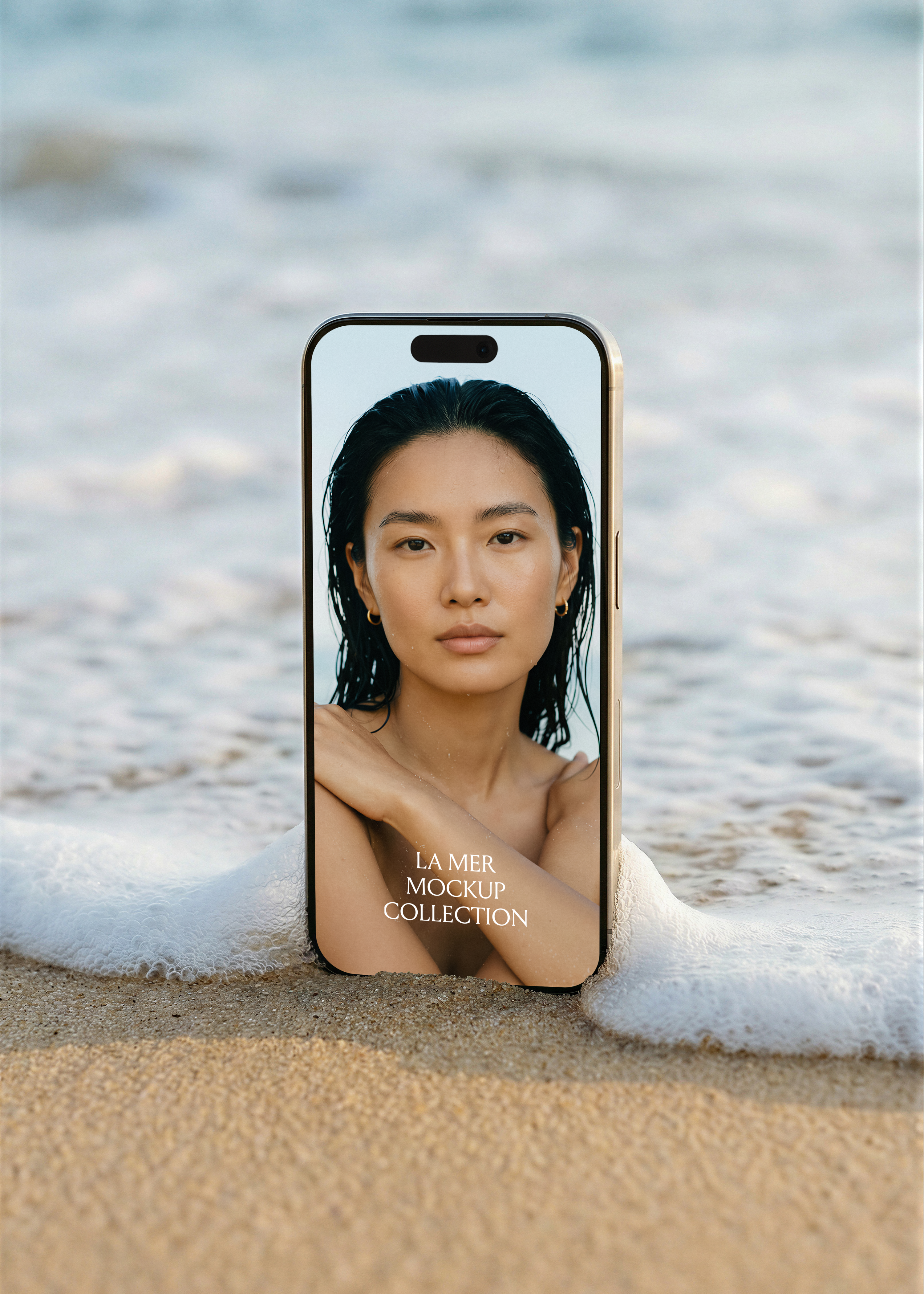 iPhone mockup on shoreline with foamy wave, front-facing editorial beauty campaign image on screen, gold frame