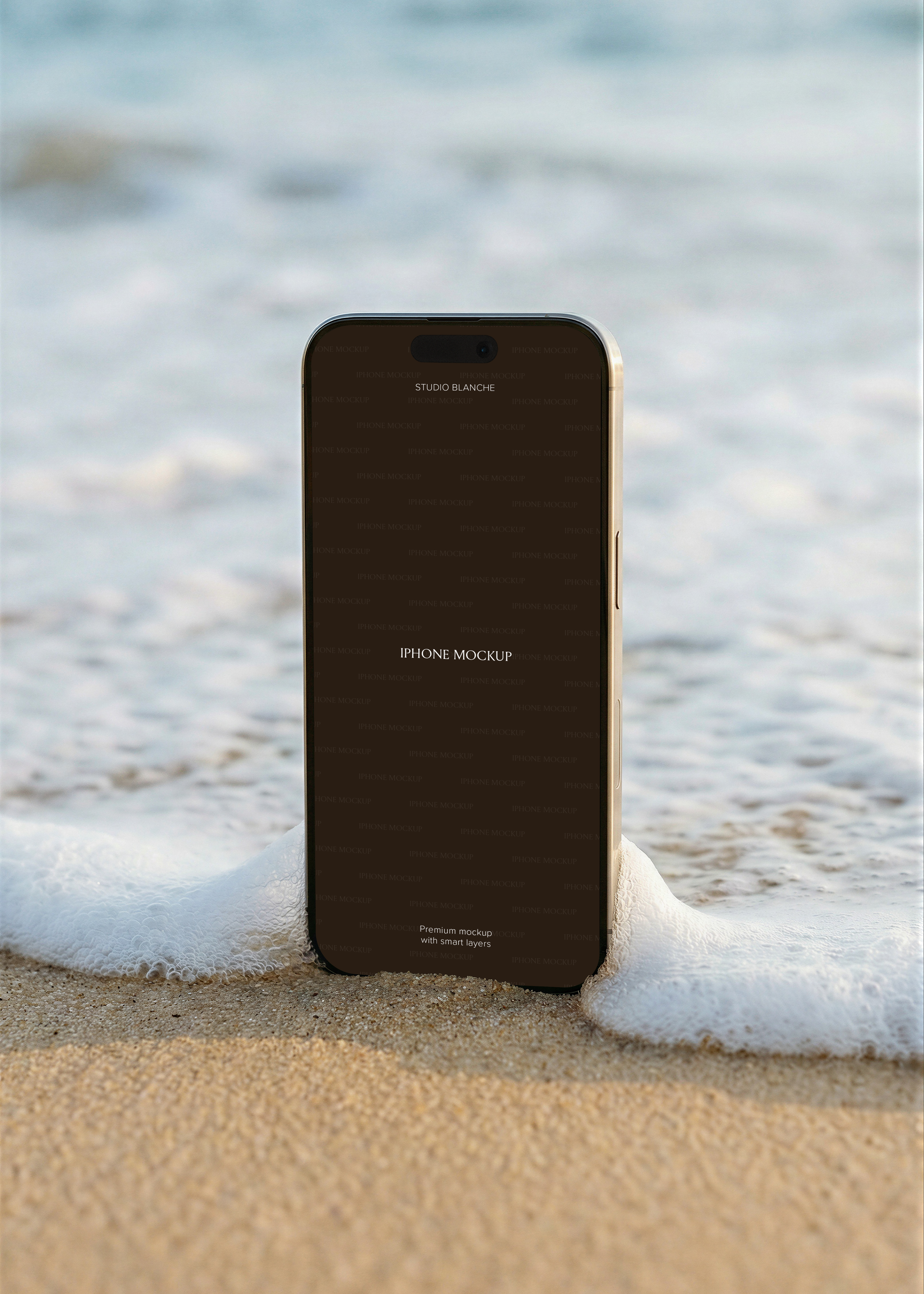 Gold iPhone standing upright on wet sand with soft wave foam at base, open ocean and blue sky in soft focus behind